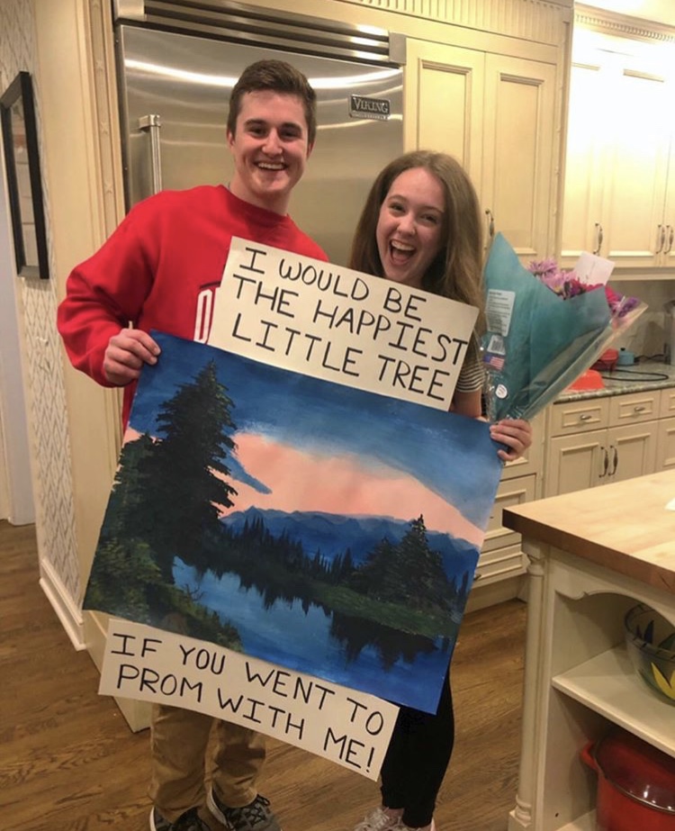 A sign that says "I would be the happiest little tree if you would go to prom with me" above a Bob Ross painting